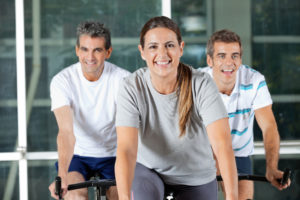 Happy men and woman on exercise bikes in health club